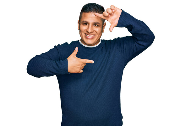 Jovem latino vestindo roupas casuais sorrindo fazendo moldura com mãos e dedos com rosto feliz. conceito de criatividade e fotografia.  - Foto, Imagem
