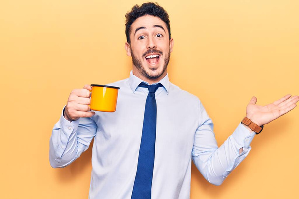Young hispanic man wearing business clothes holding coffee celebrating achievement with happy smile and winner expression with raised hand  - Foto, afbeelding