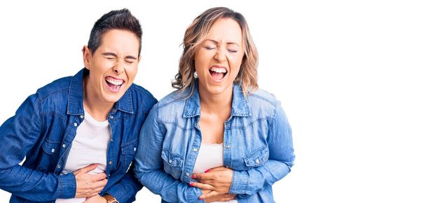 Un par de mujeres vistiendo ropa casual sonriendo y riendo en voz alta porque divertida broma loca con las manos en el cuerpo.  - Foto, Imagen