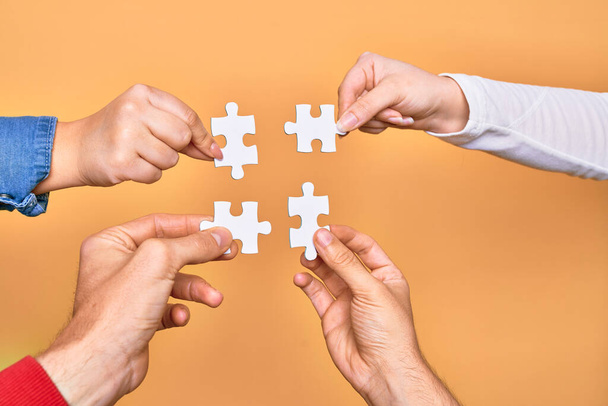 Hands of caucasian young people connecting pieces of puzzle over isolated yellow background - Photo, Image