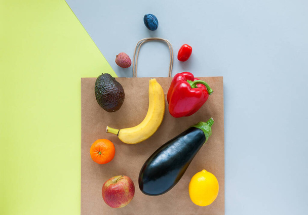 Shopping paper bag with different fruits and vegetables on it. Grey and yellow background, flat lay. - 写真・画像