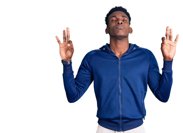 スポーツウェアを身に着けている若いアフリカ系アメリカ人の男性は、指で瞑想ジェスチャーを行う閉じて目でリラックスして笑顔。ヨガのコンセプト.  - 写真・画像
