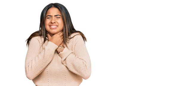 Молода латинська дівчина в шерсті зимовий светр кричить задихаючись, тому що болючий диван. проблеми зі здоров'ям. концепція асфіксії та самогубства
.  - Фото, зображення