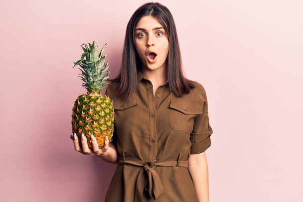 Young beautiful girl holding pineapple scared and amazed with open mouth for surprise, disbelief face  - Fotografie, Obrázek