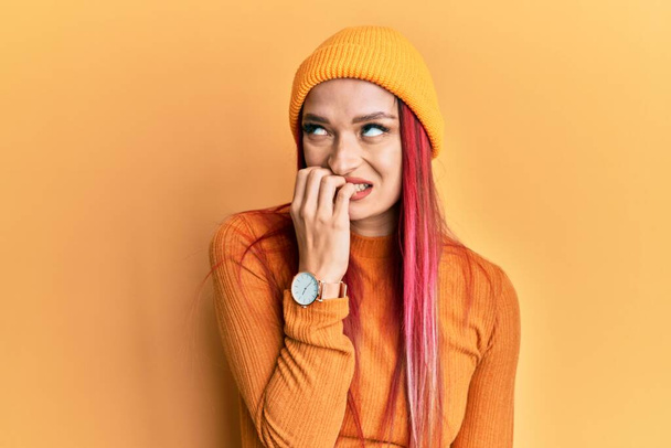 Jeune femme caucasienne portant une casquette en laine à l'air stressée et nerveuse avec les mains sur les ongles mordants. problème d'anxiété.  - Photo, image