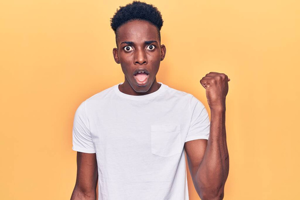 Jeune homme afro-américain portant des vêtements décontractés surpris pointant du doigt vers le côté, bouche ouverte expression étonnée.  - Photo, image