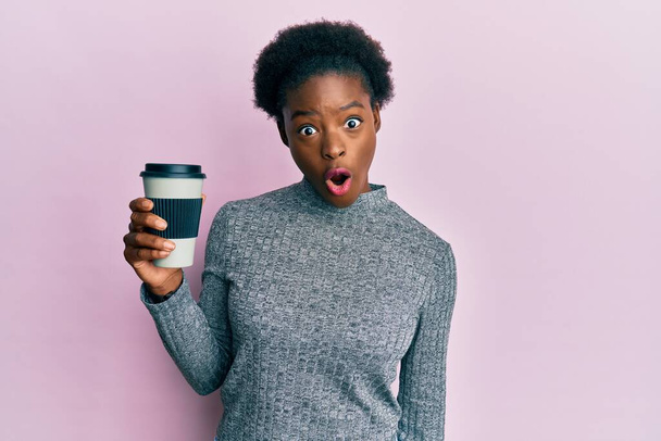 Fiatal afro-amerikai lány tartja vigye el a kávét ijedt és csodálkozott nyitott szájjal meglepetés, hitetlen arc  - Fotó, kép