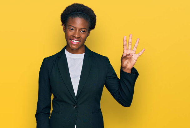 Молода афроамериканка, одягнена в діловий одяг, показує і вказує вгору пальцями номер чотири, посміхаючись впевнено і щасливо.  - Фото, зображення