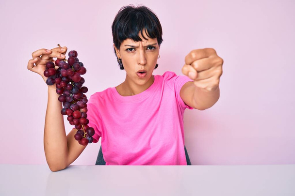 Belle femme brunettte tenant branche de raisins frais agacés et frustrés criant de colère, criant fou de colère et la main levée  - Photo, image