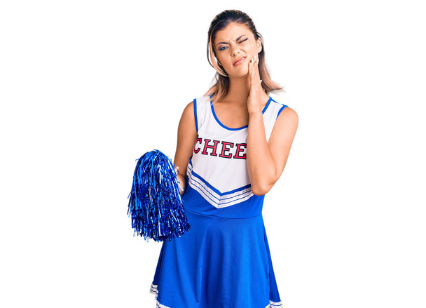 Jonge mooie vrouw dragen cheerleader uniform aanraken mond met de hand met pijnlijke uitdrukking als gevolg van kiespijn of tandheelkundige ziekte op tanden. tandartsconcept.  - Foto, afbeelding