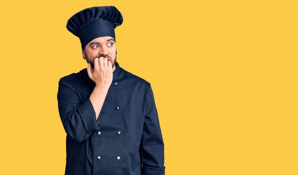 Junger hispanischer Mann in Kochuniform sieht gestresst und nervös aus, die Hände auf den Mund beißenden Nägeln. Angstproblem.  - Foto, Bild