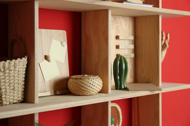 Stilvolles Holzregal mit dekorativen Elementen an roter Wand - Foto, Bild