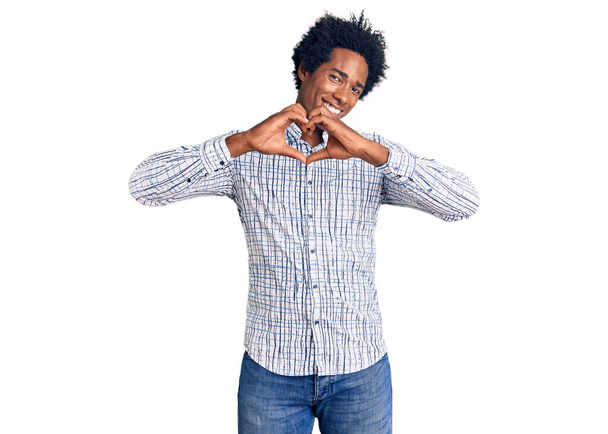 Knappe Afro-Amerikaanse man met afro-haar in casual kleding glimlachend in liefde met hartsymbool en vorm met handen. romantisch concept.  - Foto, afbeelding