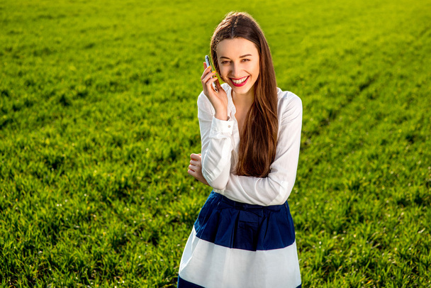 Joven mujer sonriente hablando por teléfono inteligente en el campo verde
 - Foto, imagen