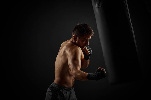 Male boxer punching in boxing bag - Foto, afbeelding