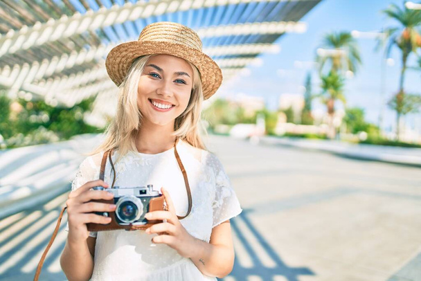 Jeune fille touristique caucasienne souriant heureux en utilisant une caméra vintage à la rue de la ville. - Photo, image