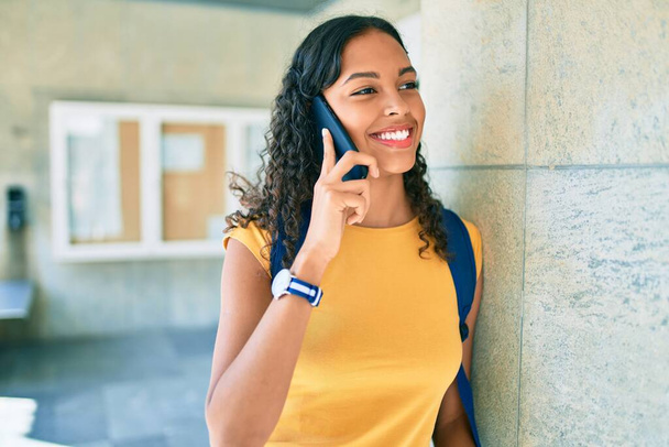 Młoda afrykańska studentka uśmiecha się szczęśliwa rozmawiając przez smartfona na uniwersytecie. - Zdjęcie, obraz