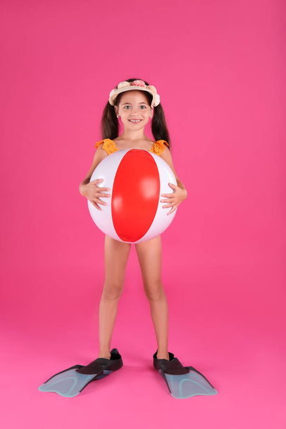Cute little child in beachwear with bright inflatable ball on pink background - Фото, зображення