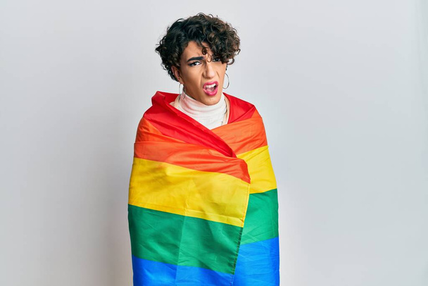 Jovem vestindo mulher compõem envolto em arco-íris lgbtq bandeira em face de choque, olhando cético e sarcástico, surpreso com a boca aberta  - Foto, Imagem