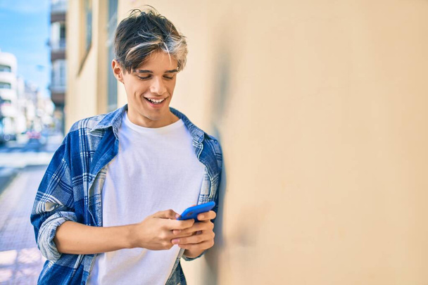 Junger hispanischer Mann lächelt glücklich mit Smartphone in die Stadt. - Foto, Bild