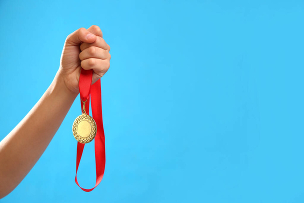 Woman holding gold medal on light blue background, closeup. Space for text - Foto, immagini