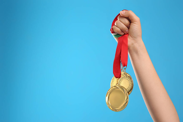 Woman holding gold medals on light blue background, closeup. Space for text - Fotografie, Obrázek