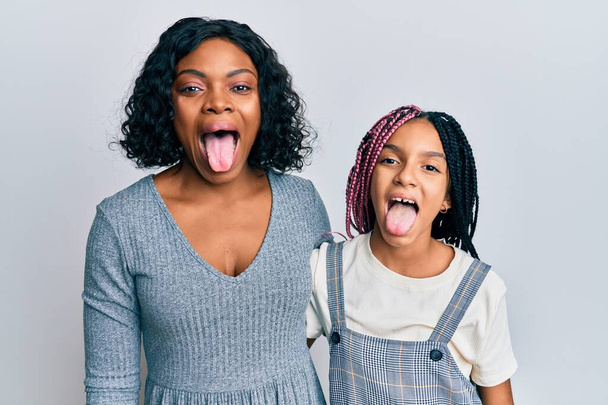 Bela mãe e filha afro-americana vestindo roupas casuais e abraçando língua furar feliz com expressão engraçada. conceito de emoção.  - Foto, Imagem