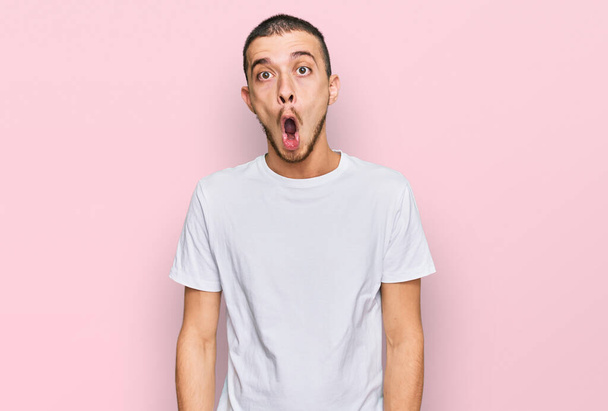 Hombre joven hispano vistiendo camiseta blanca casual asustado y sorprendido con la expresión sorpresa, el miedo y la cara emocionada.  - Foto, imagen