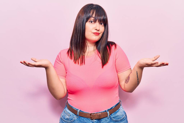 Young plus size woman wearing casual clothes clueless and confused expression with arms and hands raised. doubt concept.  - Photo, Image