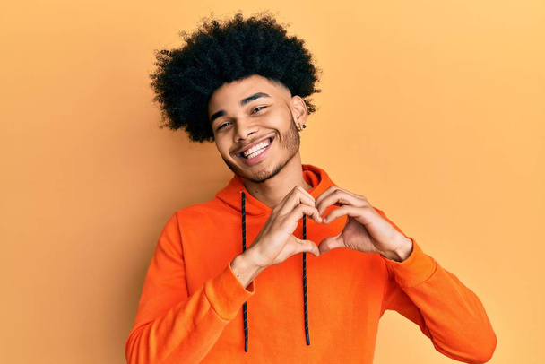 Young african american man with afro hair wearing casual sweatshirt smiling in love doing heart symbol shape with hands. romantic concept.  - Fotografie, Obrázek