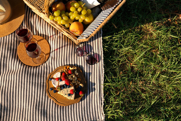 Red wine and different products for summer picnic served on blanket outdoors, flat lay - Фото, изображение