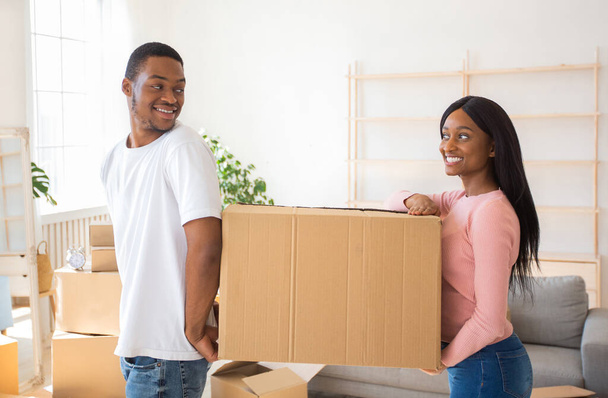 Home relocation concept. Friendly black couple with carton box relocating to new home, copy space - Foto, Imagen