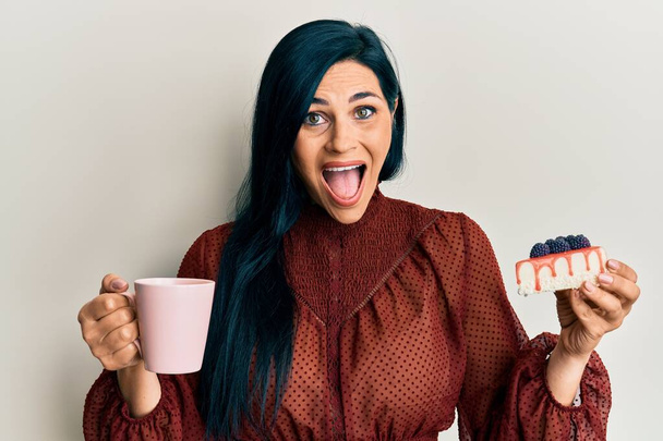 Young caucasian woman holding cup of coffee and cake slice celebrating crazy and amazed for success with open eyes screaming excited.  - Foto, immagini