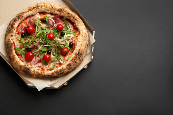 Tasty pizza with meat and arugula in cardboard box on black background, top view. Space for text - Foto, afbeelding