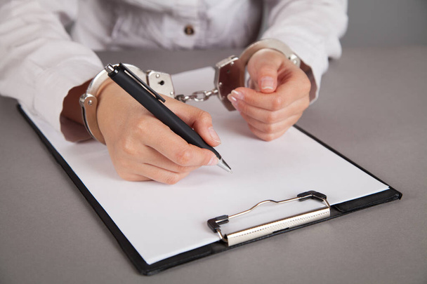 Woman fills out documents with handcuffs. - Foto, imagen