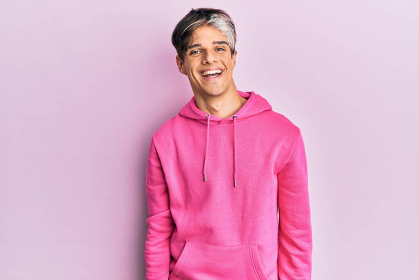 Молодой латиноамериканец в обычной розовой толстовке со счастливой и прохладной улыбкой на лице. счастливчик.  - Фото, изображение