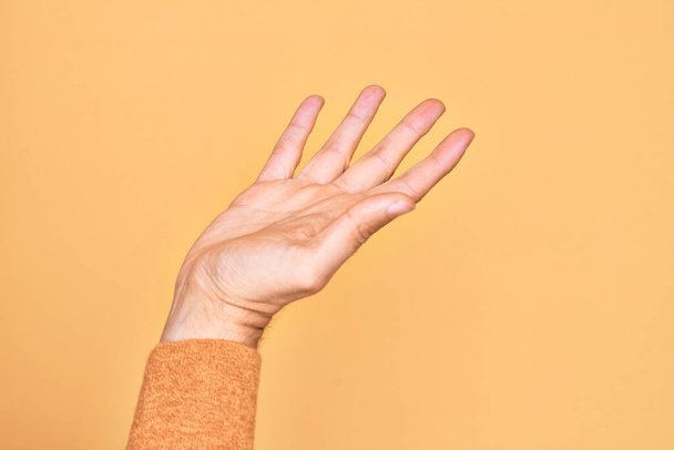 Ruka kavkazského mladíka ukazující prsty na izolovaném žlutém pozadí s otevřenou dlaní, natahující se pro podporu a pomoc, asistenční gesto - Fotografie, Obrázek