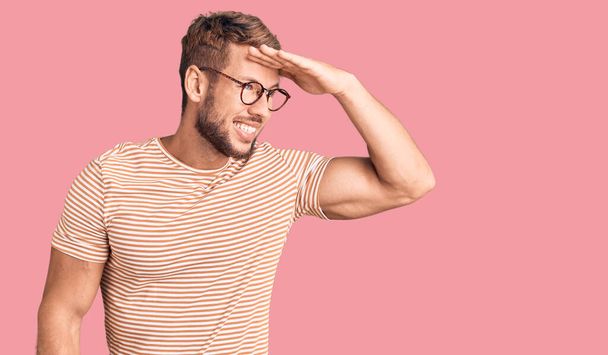Young caucasian man wearing casual clothes and glasses very happy and smiling looking far away with hand over head. searching concept.  - Photo, Image