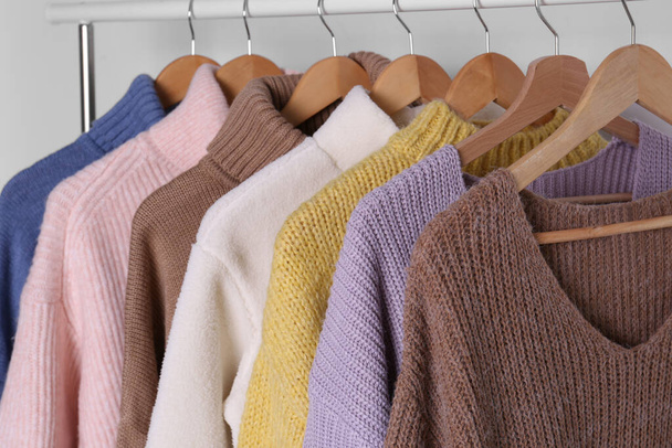Warm sweaters hanging on rack against white background, closeup - Fotó, kép