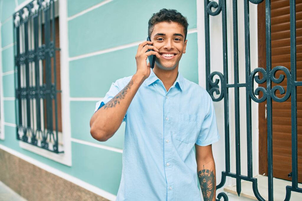 Joven latino sonriendo feliz usando smartphone caminando por la ciudad. - Foto, Imagen