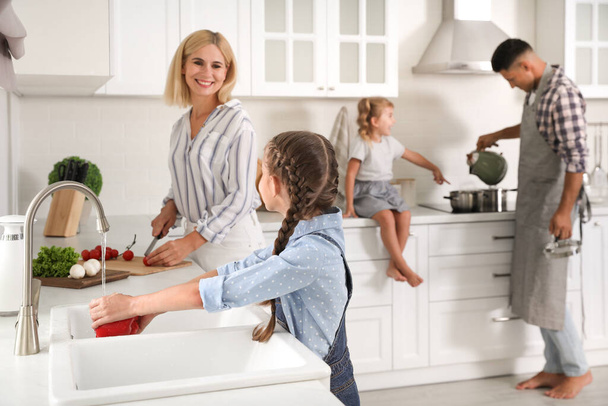 Little girl with her mother washing vegetables together in modern kitchen - Zdjęcie, obraz