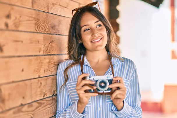 Młoda latynoska turystka uśmiechnięta szczęśliwa używając zabytkowej kamery w mieście. - Zdjęcie, obraz
