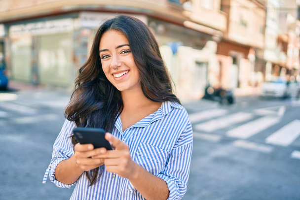 Mladá hispánská obchodnice se šťastně usmívá pomocí smartphonu ve městě. - Fotografie, Obrázek