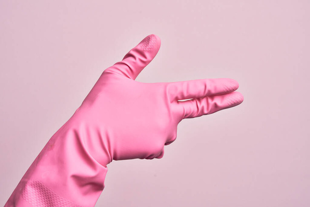 孤立したピンクの背景の上に手袋を掃除している白人青年の手指で銃の武器をジェスチャー,撮影シンボルを目指して - 写真・画像