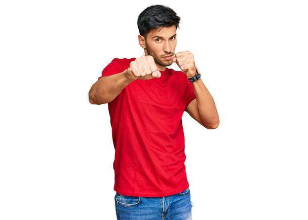 Genç, yakışıklı bir adam gündelik kırmızı tişört giyiyor dövüşmek için yumruk atıyor agresif ve öfkeli saldırı, tehdit ve şiddet.  - Fotoğraf, Görsel