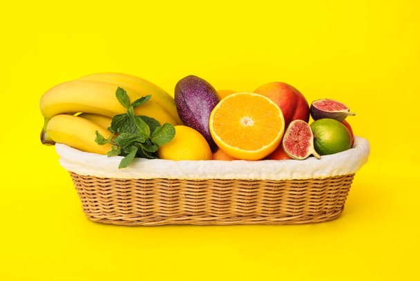 Assortment of fresh exotic fruits in basket on yellow background - 写真・画像