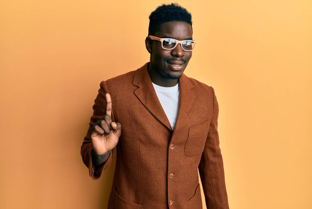 Handsome black man wearing elegant clothes and glasses smiling with an idea or question pointing finger up with happy face, number one  - Foto, imagen