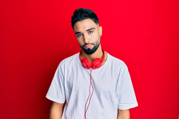 Young man with beard listening to music using headphones looking sleepy and tired, exhausted for fatigue and hangover, lazy eyes in the morning.  - Photo, image