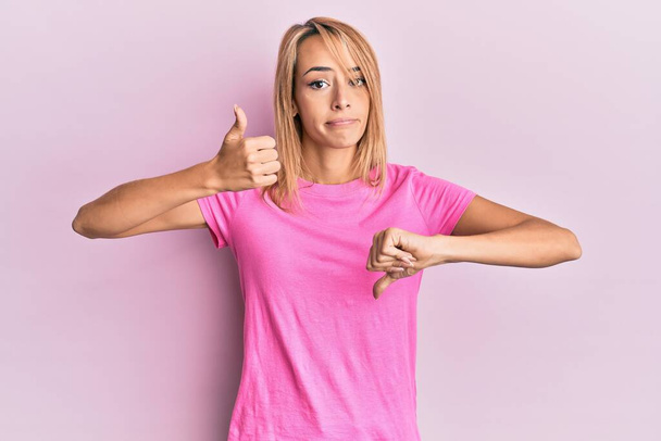 Hermosa mujer rubia con camiseta rosa casual haciendo pulgares arriba y abajo, desacuerdo y expresión de acuerdo. conflicto loco  - Foto, Imagen