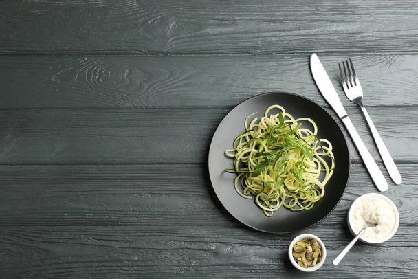 Delicious zucchini pasta with arugula, pumpkin seeds and sauce served on grey wooden table, flat lay. Space for text - Φωτογραφία, εικόνα